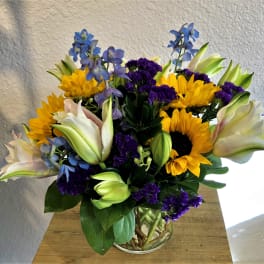 Bouquet of sunflowers, lilies, and purple flowers in a glass vase