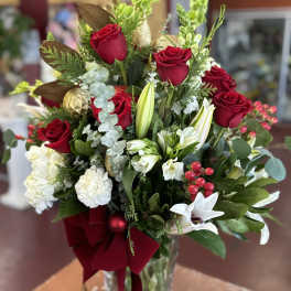 Red roses and white lilies in a clear glass vase with a burgundy ribbon.