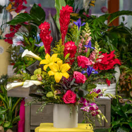 Tropical bouquet with yellow lilies, pink roses, and red ginger in a white vase