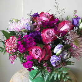 Bouquet of pink and purple roses, chrysanthemums, and carnations in a green vase