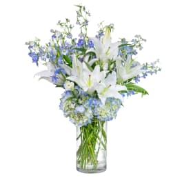 White lilies and blue flowers arranged in a clear glass vase