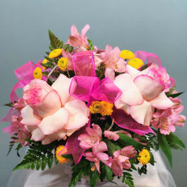 Pink and yellow mixed flower arrangement with roses and alstroemeria in a white basket with bright pink ribbon bows