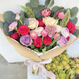 Bouquet of pink, cream, and lavender flowers wrapped in burlap with a ribbon