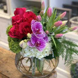 Bright pink roses, tulips and speckled orchids with white blooms in a round glass vase