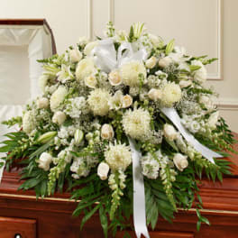 White funeral spray with lilies, roses, and ribbons on a casket