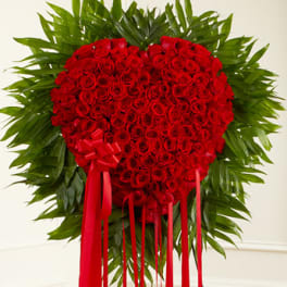 Heart-shaped red rose arrangement with a red ribbon and palm leaves