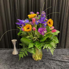 Colorful bouquet of sunflowers, irises, tulips, and purple flowers in a glass vase