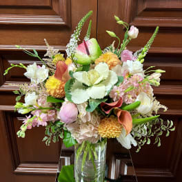 Tall mixed bouquet of pink, peach, yellow, and white flowers in a clear glass vase.
