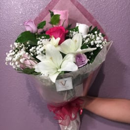 Wrapped bouquet of white lilies and mixed pink and purple roses held against a purple wall