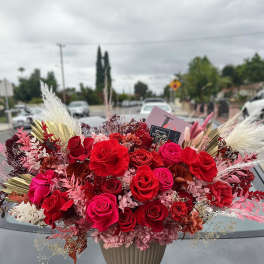 Large red and pink rose arrangement in a beige vase