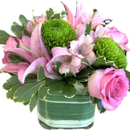 Compact arrangement of pink lilies and roses with green mums in a striped green glass vase