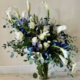 Tall bouquet of white calla lilies, roses, and blue flowers in a glass vase