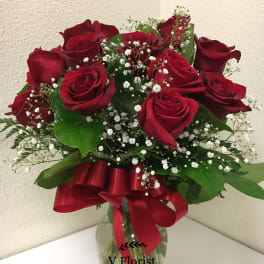 Arrangement of red roses and white filler flowers in a clear glass vase with a red bow