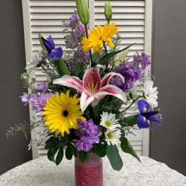 Mixed bouquet of lilies, daisies, and purple flowers in a tall glass vase