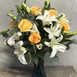 Arrangement of yellow roses and white lilies in a blue glass vase