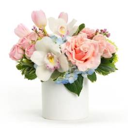 Pastel bouquet of pink roses, tulips, white orchids, and blue hydrangea in a white vase