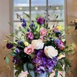 Arrangement of purple hydrangeas, pink and white roses, and mixed blooms in a metal bucket-style vase