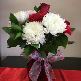 Red and white bouquet with roses, carnations and mums in a red vase with heart ribbon