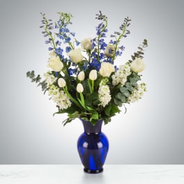 Tall arrangement of white roses, tulips, and blue flowers in a cobalt blue glass vase
