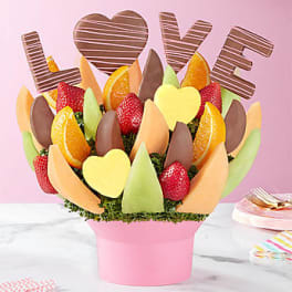 Fruit and chocolate bouquet in a pink box with "LOVE" letters behind it