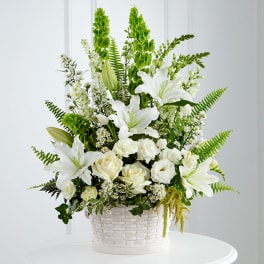 White lilies and roses arranged in a white basket with green accents