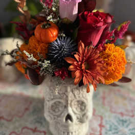 Autumn bouquet in a skull vase with roses, mums, and a small pumpkin