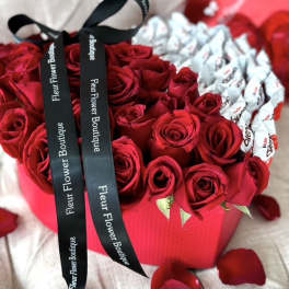 Red roses arranged in a heart-shaped box with black ribbons