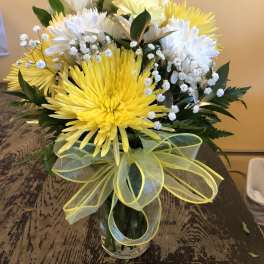 Yellow and white chrysanthemum bouquet in a glass vase with a ribbon