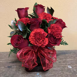 Red rose and carnation arrangement in a black vase with a red ribbon