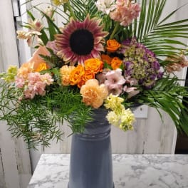 Mixed bouquet in a tall blue vase with sunflowers, roses, and lilies