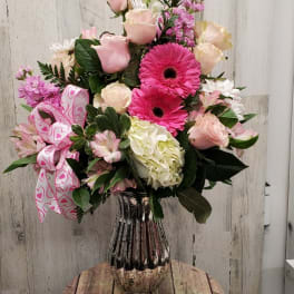 Pink and white mixed flower arrangement in a glass vase with a heart ribbon