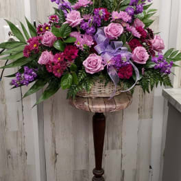 Pink and purple floral arrangement in a wicker basket on a wooden stand