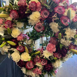 Heart-shaped floral wreath with pink roses and white carnations on an easel