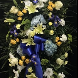 Standing floral wreath with lilies, roses, hydrangeas, and a blue ribbon