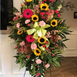 Standing floral spray with sunflowers, pink gerberas, and carnations on an easel
