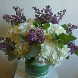 White hydrangeas and purple lilacs in a green-striped vase