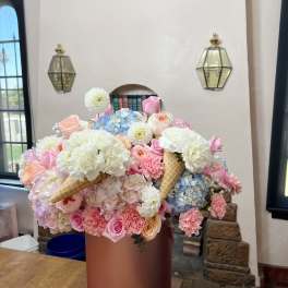 Large pastel flower arrangement in a round pink box with ice cream cone accents