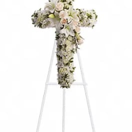 White floral cross on a stand with lilies and roses