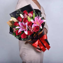 Bouquet of red roses and pink lilies wrapped in black paper with a red ribbon