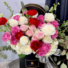 Round box arrangement of red, pink, and white roses with carnations