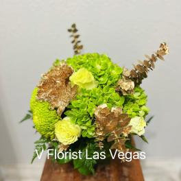 Green and pale yellow floral arrangement with gold accents in a wooden container