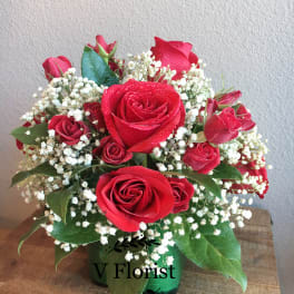 Compact arrangement of red roses and baby's breath in a green glass vase