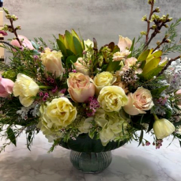Low compote arrangement of cream and blush roses with pastel blooms in a green pedestal bowl