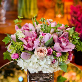Low cube vase arrangement of pink orchids, roses, and white hydrangeas on a mirrored base.