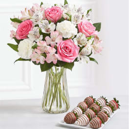 Pink and white bouquet in a clear glass vase with chocolate-covered strawberries on a tray