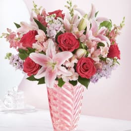 Pink lilies and red roses arranged in a striped glass vase