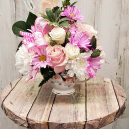 Pink and white flower arrangement in a floral teacup vase with a ribbon