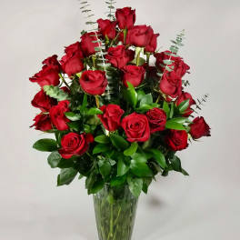 Red roses arranged in a clear glass vase with eucalyptus accents