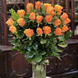 Tall arrangement of orange roses in a clear glass vase with a green ribbon bow.