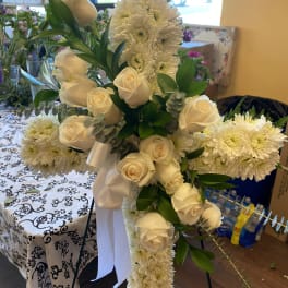 White roses and chrysanthemums arranged on a standing cross with a white ribbon.